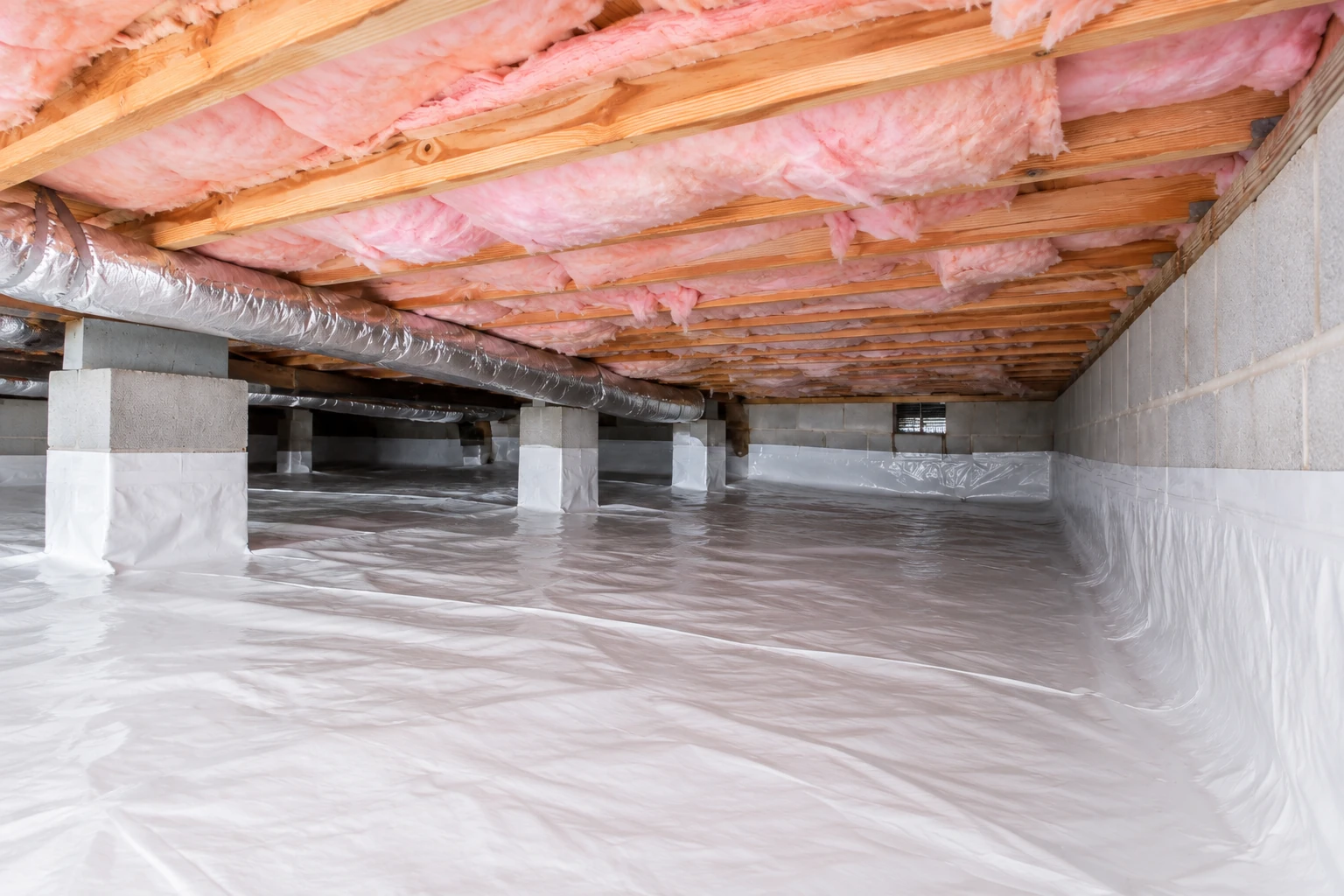 Crawl space with pink insulation between overhead joists, a silver duct, support piers, and a white floor vapor barrier.